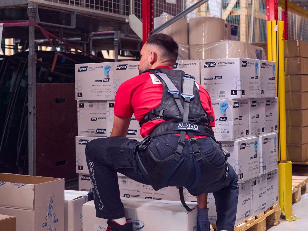 Raktári dolgozó Auxivo LiftSuit exoskeletonban dobozokat rak a raklapra